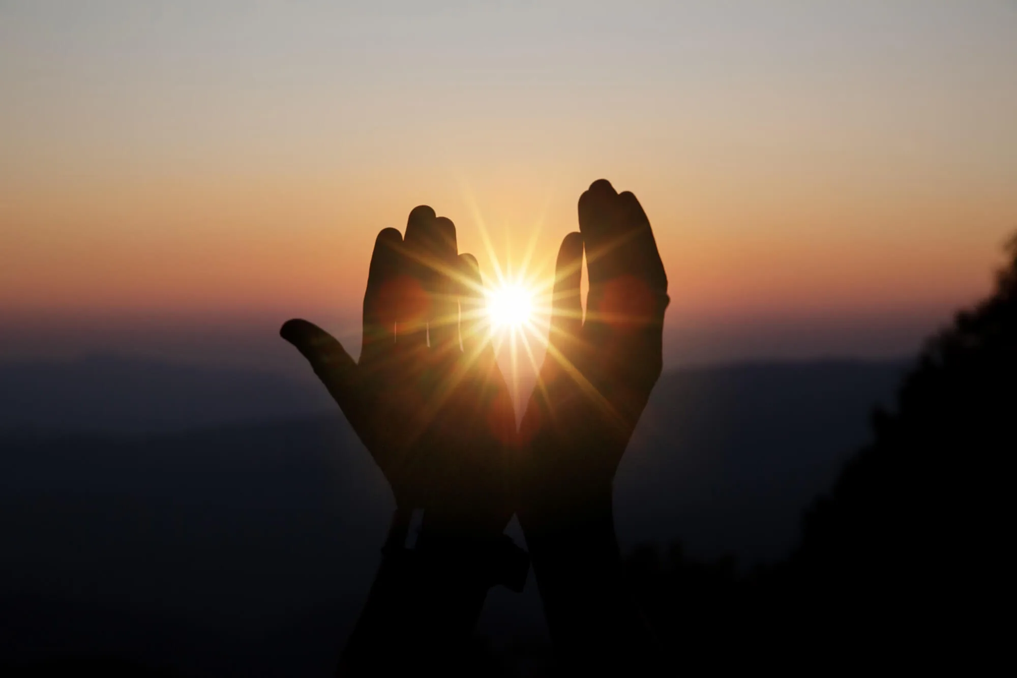 Hände vor der untergehenden Sonne als Symbol für Burnout und emotionale Erschöpfung